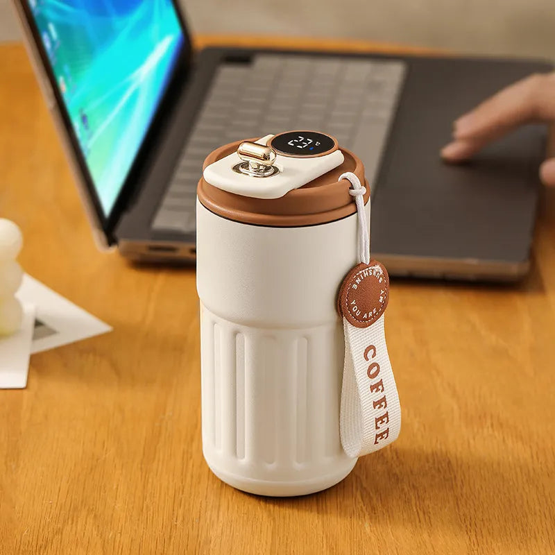 White coffee thermos with brown lid on a wooden desk next to a laptop