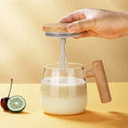 Hand using a hand mixer to blend ingredients in a glass on a yellow background