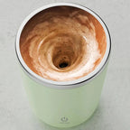 Green coffee maker with a swirling brown liquid inside on a light gray background