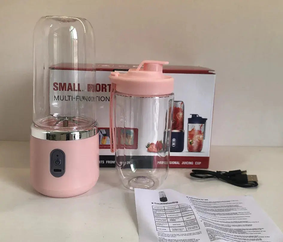 Pink portable blender with clear container on a white surface, with packaging and user manual in the background.