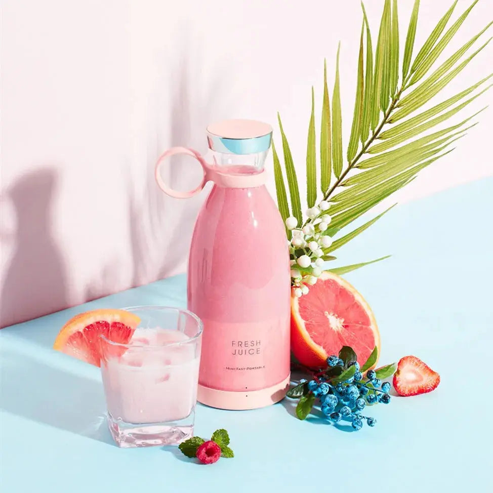 Pink juice bottle with a glass of pink juice, grapefruit, and strawberry on a light blue background
